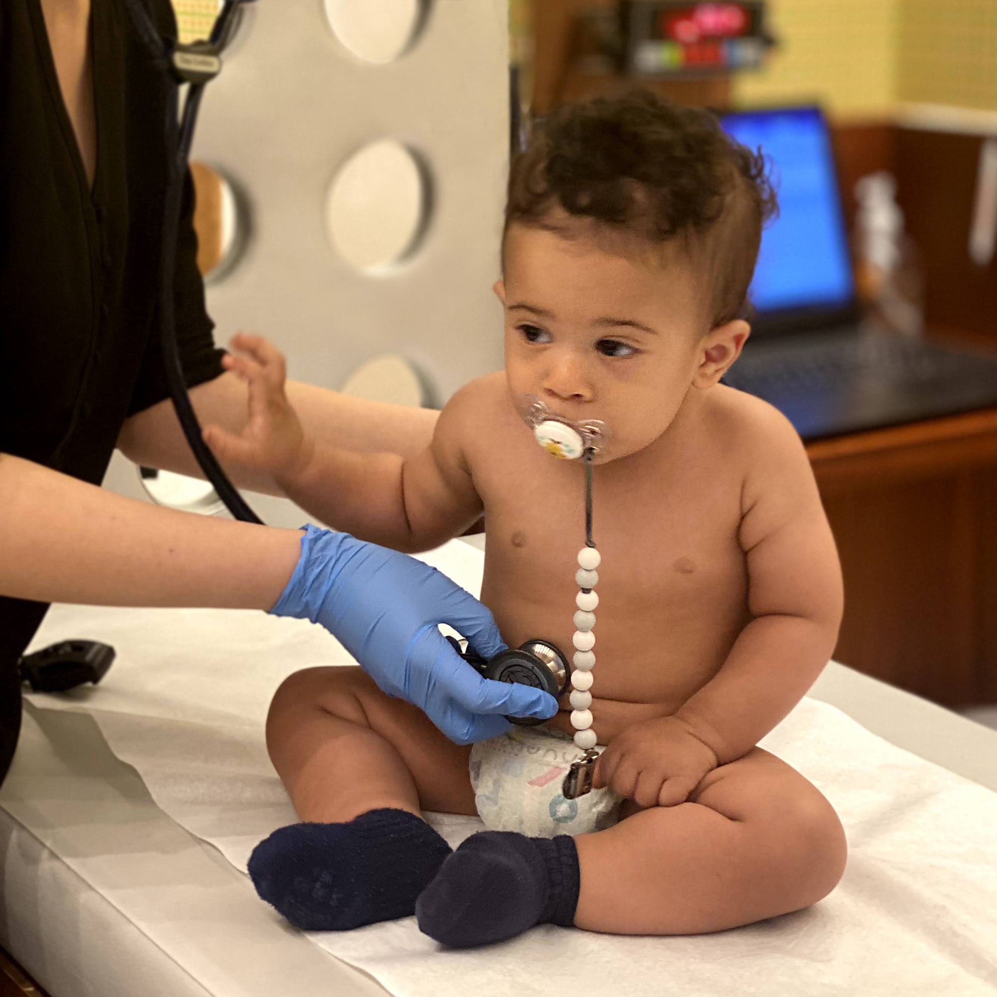 Doctor listening to baby's lungs with a stethoscope on exam table at Tribeca Pediatrics office